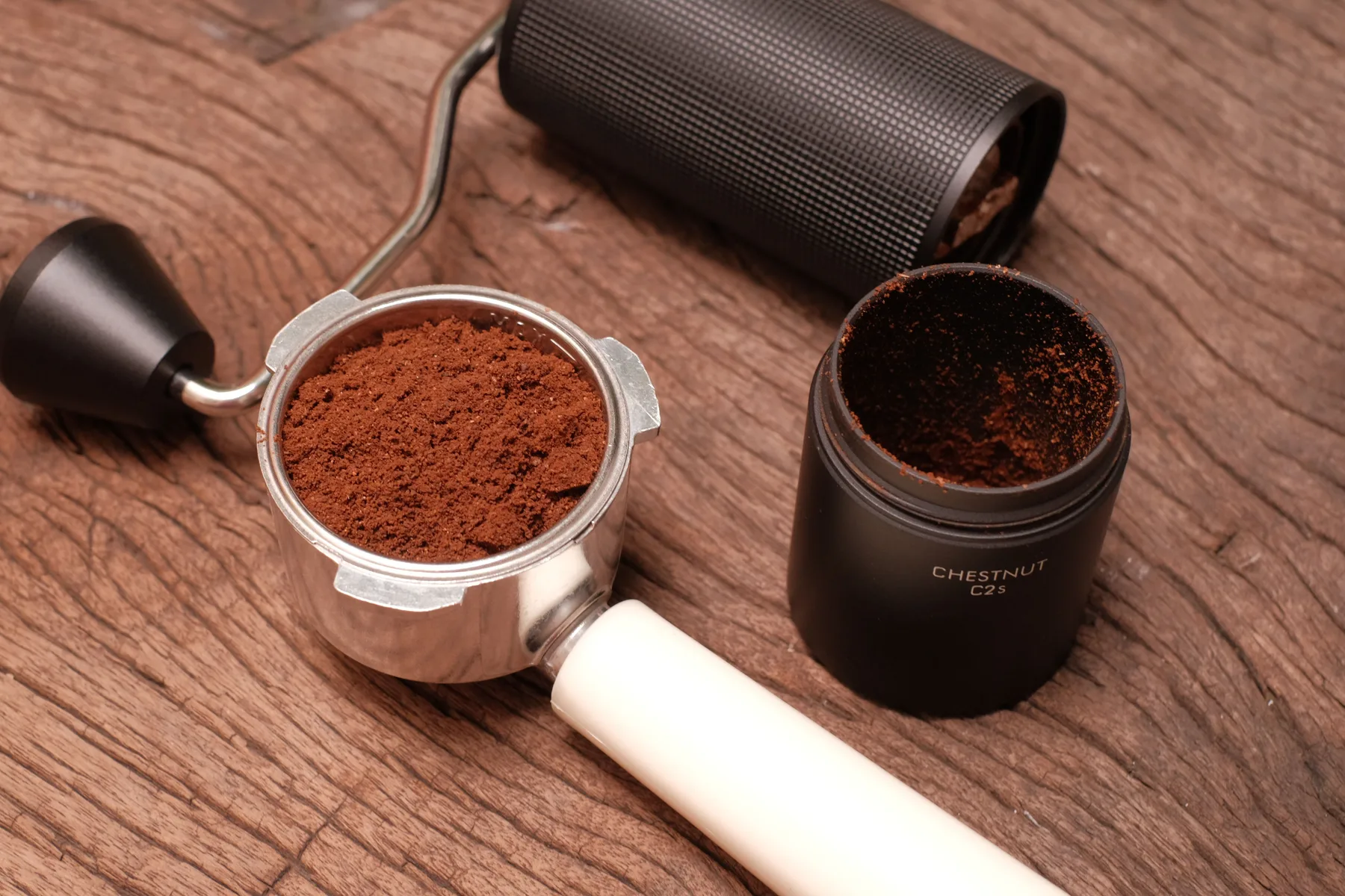 A burr grinder beside freshly ground coffee on a light surface