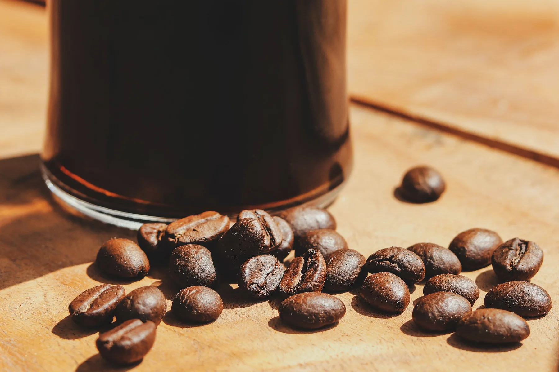 Dark brewed coffee in a clear vessel beside roasted beans